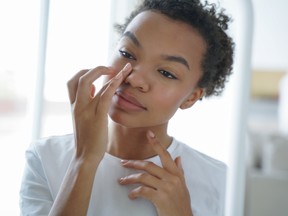 Attractive afro girl is applying cream touching her face. Femininity and grooming concept. Mirror reflection of young latin woman. Skin cleansing. Daily routine, cosmetics and hygiene of teenage girl.