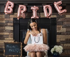 Young smiling woman opening a present at her bridal shower n her home. Pink bride balloons in background