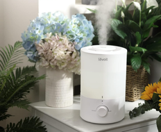 Humidifier on a table in front of a vase of flowers surrounded by greenery