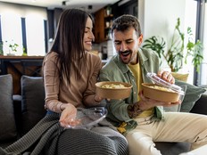 Couple eating takeout on their couch.