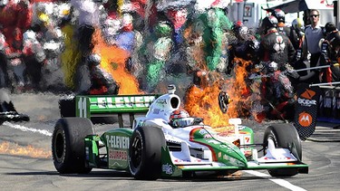 Fire breaks out on Tony Kanaan's car and pit area (in back) after a routine pit stop at the Rexall Edmonton Indy at the City Centre Airport in Edmonton, July 26, 2009. Kanaan is visibly tossing his steering wheel out of the cockpit as he is about to exit the car.