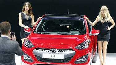 Hostesses pose next to a Hyundai i30 family car during the press day at the Paris Auto Show.