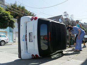 Shelley Gallivan, foreground right, looks into a tipped-over Smart car which belongs to her friend on the corner of Prospect and Coso Avenues in San Francisco, Monday, April 7, 2014. Police in San Francisco are investigating why four Smart cars were flipped over during an apparent early morning vandalism spree.