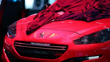 A protective cover sits over the hood of a red Peugeot RCZ R automobile, produced by PSA Peugeot Citroen, on the company's stand ahead of the opening day of the 84th Geneva International Motor Show in Geneva, Switzerland, on Monday, March 3, 2014.