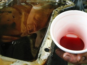 Mechanic Greg Kozak holds a transmission oil pan with black burnt oil. The cup has new transmission oil which is red.