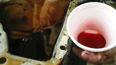 Mechanic Greg Kozak holds a transmission oil pan with black burnt oil. The cup has new transmission oil which is red.