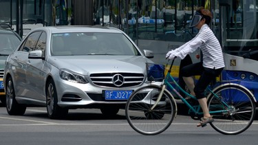 A woman rides her bicycle past a Mercedes-Benz at a cross road in Beijing.