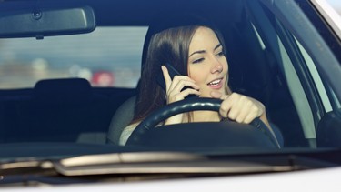 A woman talks on her phone while driving.