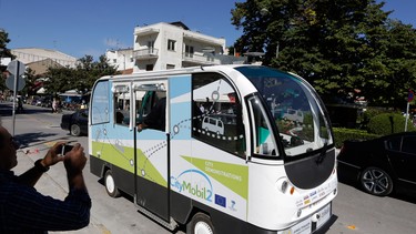 In this photo taken on Tuesday, Oct. 6, 2015, a local resident takes a photo of the tiny CityMobil2 driverless bus in Trikala town, Greece. Trials of the French-built CityMobil2 buses have started in Trikala, a town of some 80,000 people, chosen to test a driverless bus in real traffic conditions for the first time, as part of a European project to revolutionize mass transport, guided by GPS, lasers, and wireless cameras, and the rides are free.
