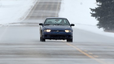 A car drives through the blowing snow on Secondary Highway 651 near Legal, Alta. on Wednesday, Feb. 11, 2015.