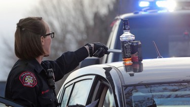 Police remove a bottle of Jack Daniels from the vehicle of a male after they performed a breathalyzer test on him on Parkhill Street in SW Calgary, Alta. on Tuesday November 17, 2015.