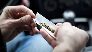 A man makes a marijuana joint inside a car.