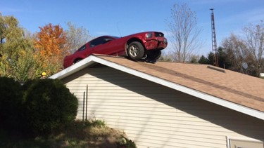 In this Oct. 26, 2015 photo, a Ford Mustang is stopped on a roof of a house in Woodhull Township, Mich. Police say the driver had a medical problem and lost control of his car.