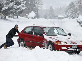 Alex Vlasity helps push out a passing car which became bogged on an unplowed road after a night of heavy snowfall, in Boulder, Colo., Tuesday, Dec. 15, 2015. The biggest winter storm to hit the Denver area so far this season has left most schools closed and created some havoc on the roads for those forced to commute.