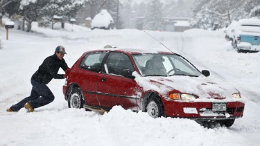 Alex Vlasity helps push out a passing car which became bogged on an unplowed road after a night of heavy snowfall, in Boulder, Colo., Tuesday, Dec. 15, 2015. The biggest winter storm to hit the Denver area so far this season has left most schools closed and created some havoc on the roads for those forced to commute.