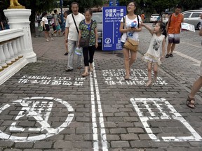 In this photo taken Saturday, Sept. 13, 2014, residents walk on a lane painted with instructions to separate those using their phones as they walk from others in southwest China's Chongqing Municipality. The Chinese city took a cue from a U.S. TV program and created a sidewalk with a separate lane for those with heads tucked into smartphones, as a reminder not to tweet while walking the street.