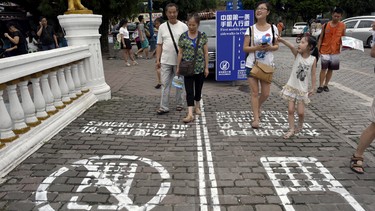 In this photo taken Saturday, Sept. 13, 2014, residents walk on a lane painted with instructions to separate those using their phones as they walk from others in southwest China's Chongqing Municipality. The Chinese city took a cue from a U.S. TV program and created a sidewalk with a separate lane for those with heads tucked into smartphones, as a reminder not to tweet while walking the street.