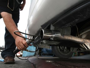 A worker inserts a probe into the tailpipe of a car while performing an emissions test