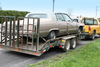 A classic Cadillac on a flatbed trailer, being towed by a truck