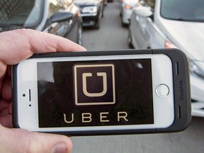 A person holds a mobile phone with the Uber app showing on it.