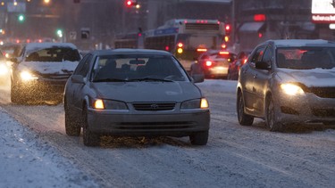 A car without headlights is driven along 109 Street in a snowstorm in Edmonton, Alberta on Friday, Jan. 26, 2018.