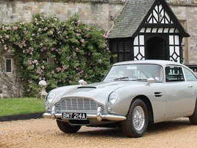 Silver classic Aston Martin parked in front of a stone-faced cottage