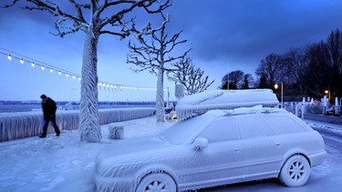 In this file photo, a man walks past an ice-covered car on the frozen waterside promenade at Lake Geneva in the city Versoix, near Geneva on early February 2012.