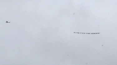 A pilot flies a banner over Ford headquarters with the caption "Is a Ford GT in my future? #GoingFurther"