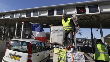 A demonstrator wearing a yellow vest waves a French flag as protesters open the toll gates on a motorway near Aix-en-Provence, southeastern France, Tuesday, Dec. 4, 2018.