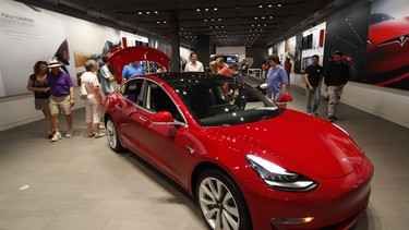 In this July 6, 2018 file photo, prospective customers confer with sales associates as a Model 3 sits on display in a Tesla showroom in the Cherry Creek Mall in Denver.