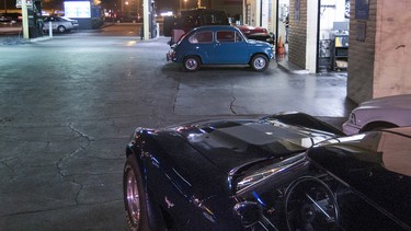 A Corvette Stingray and Fiat 600 parked beside a gas station pump at night.