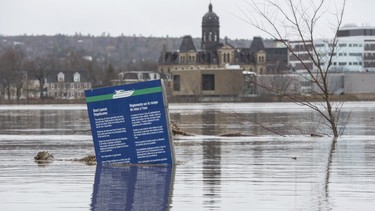 The New Brunswick Legislature is seen in the background of a boat ramp sign in Carleton Park surrounded by the flood water and debris from the St. John River in Fredericton, N.B. on Saturday, April 20, 2019.