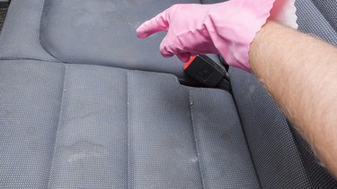 Man's hand in rubber protective glove with finger pointing to dirty textile back seat. Car's interior problem and solution. Cleaning concept.