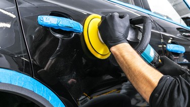 A car detailer buffs the paint on a black car.