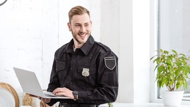 handsome policeman smiling and using laptop at kitchen