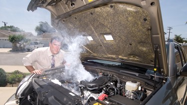 A man is very frustrated and sweaty while trying to evaluate his smoking car engine.