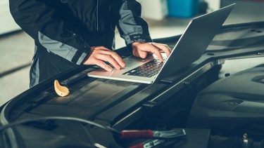 Car Mechanic with Laptop Computer Placed Near the Vehicle Engine