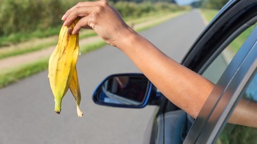 Female arm throwing  fruit waste out of car window.