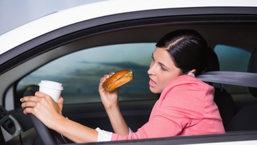 Woman drinking coffee and eating sandwich on phone in her car