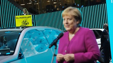 German Chancellor Angela Merkel speaks at the BMW stand while a Greenpeace activist protests against the auto industry behind on the opening day of the IAA 2019 Frankfurt Auto Show on September 12, 2019 in Frankfurt am Main, Germany.