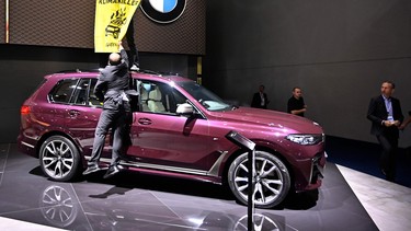 A Greenpeace activist standing on a BMW car holds a poster reading "Climate Killers" as she demonstrates at the booth of German car maker BMW during the 2019 IAA in Frankfurt.