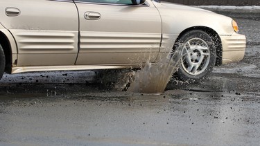 A car hits a pothole on a city street, throwing up water and debris.