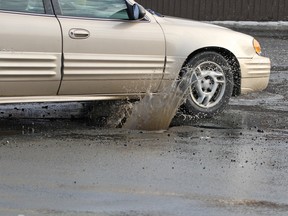 A car hits a pothole on a city street, throwing up water and debris.