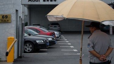 A security guard stands under an umbrella at an Audi car seller in Shanghai on August 6, 2014.