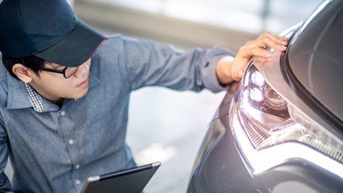Young auto mechanic holding digital tablet checking headlight in auto service garage. Mechanical maintenance engineer working in automotive industry. Automobile servicing and repair concept