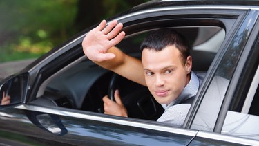 portrait of young man driving car and greeting somebody