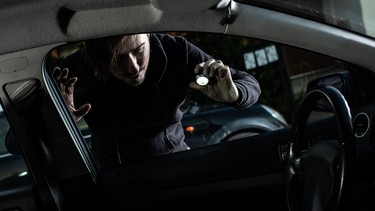 Masked thief in a balaclava looking to car interior with flashlight