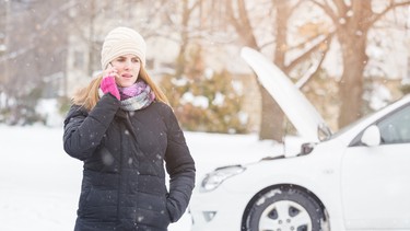 Female standing next to broken car and talking on mobile phone.