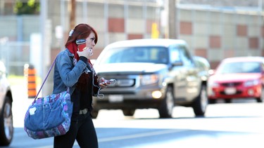 In this file photo, a woman wearing headphones crosses the street at a Toronto intersection.