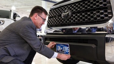 Minister of Government and Consumer Services and Bruce-Grey-Owen Sound MPP Bill Walker holds up a new Ontario commercial vehicle licence plate on the front bumper of a truck.